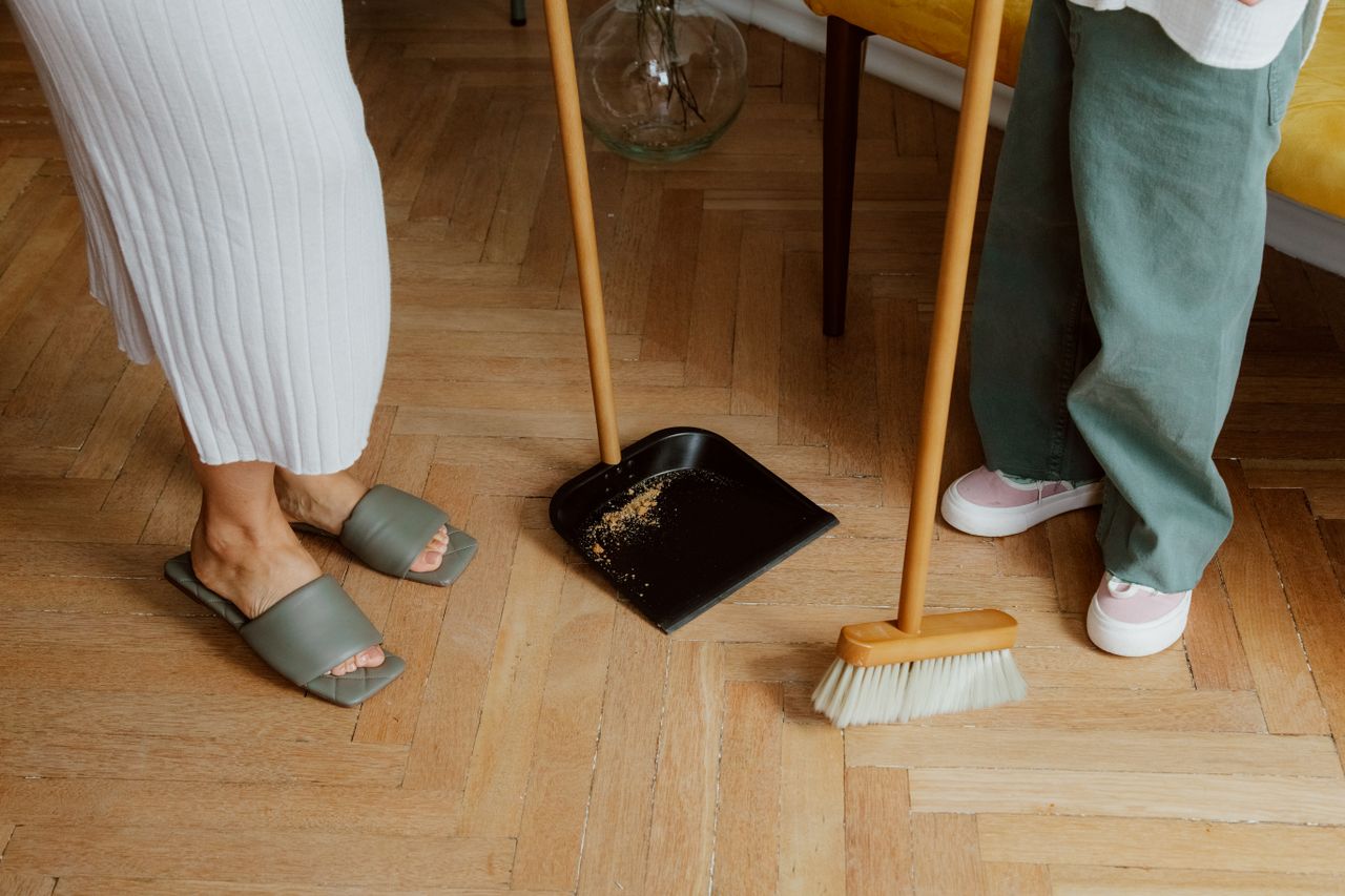 services-01 A mother and child cleaning the floor with a broom and dustpan indoors.