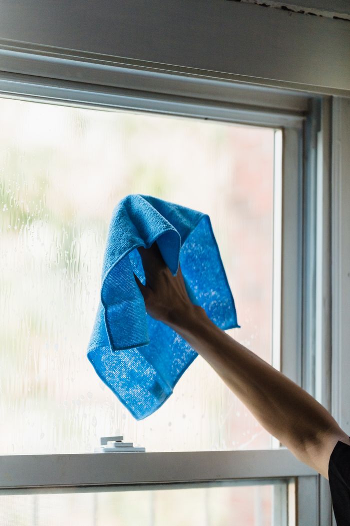 hero-01 A hand using a blue towel to clean a window indoors, showcasing housework.